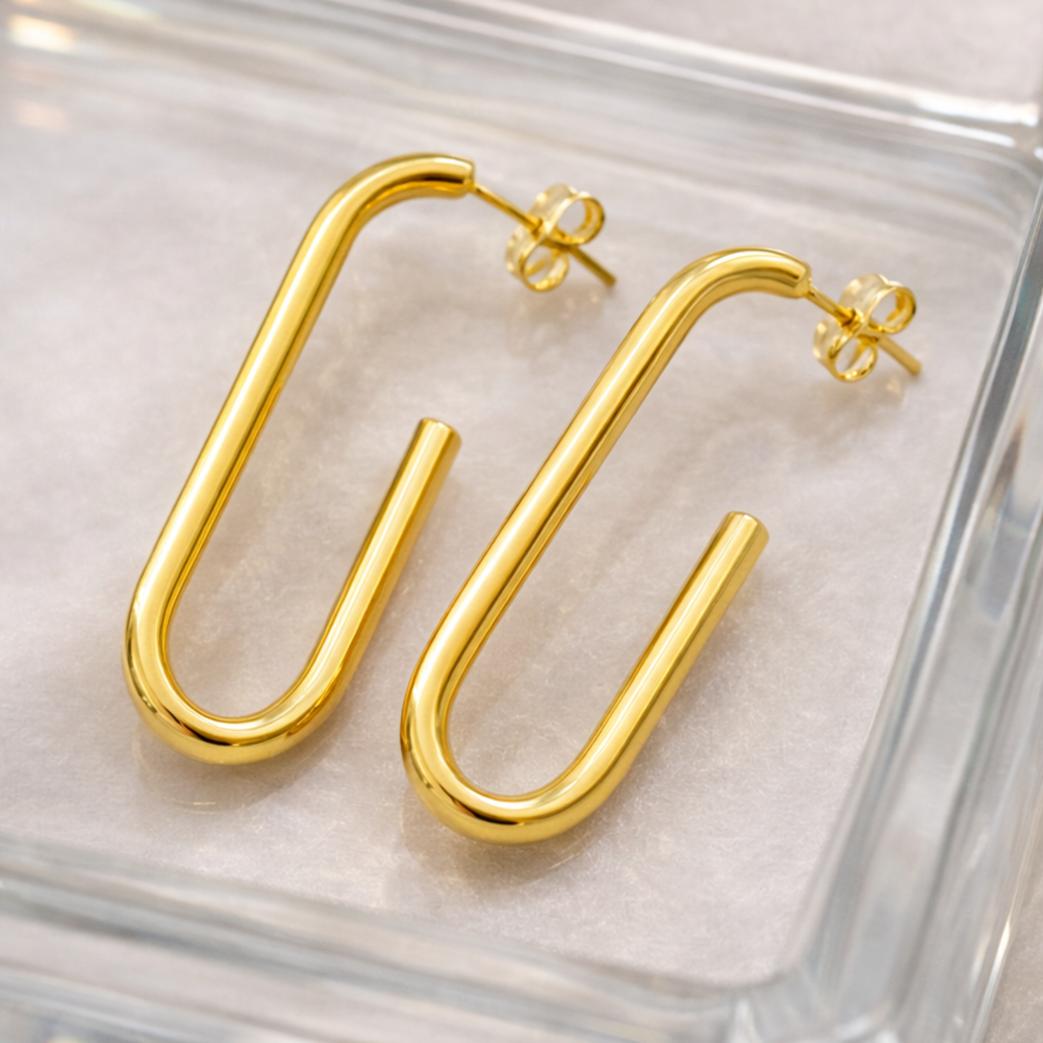 Gold hoop earrings on a clear glass surface