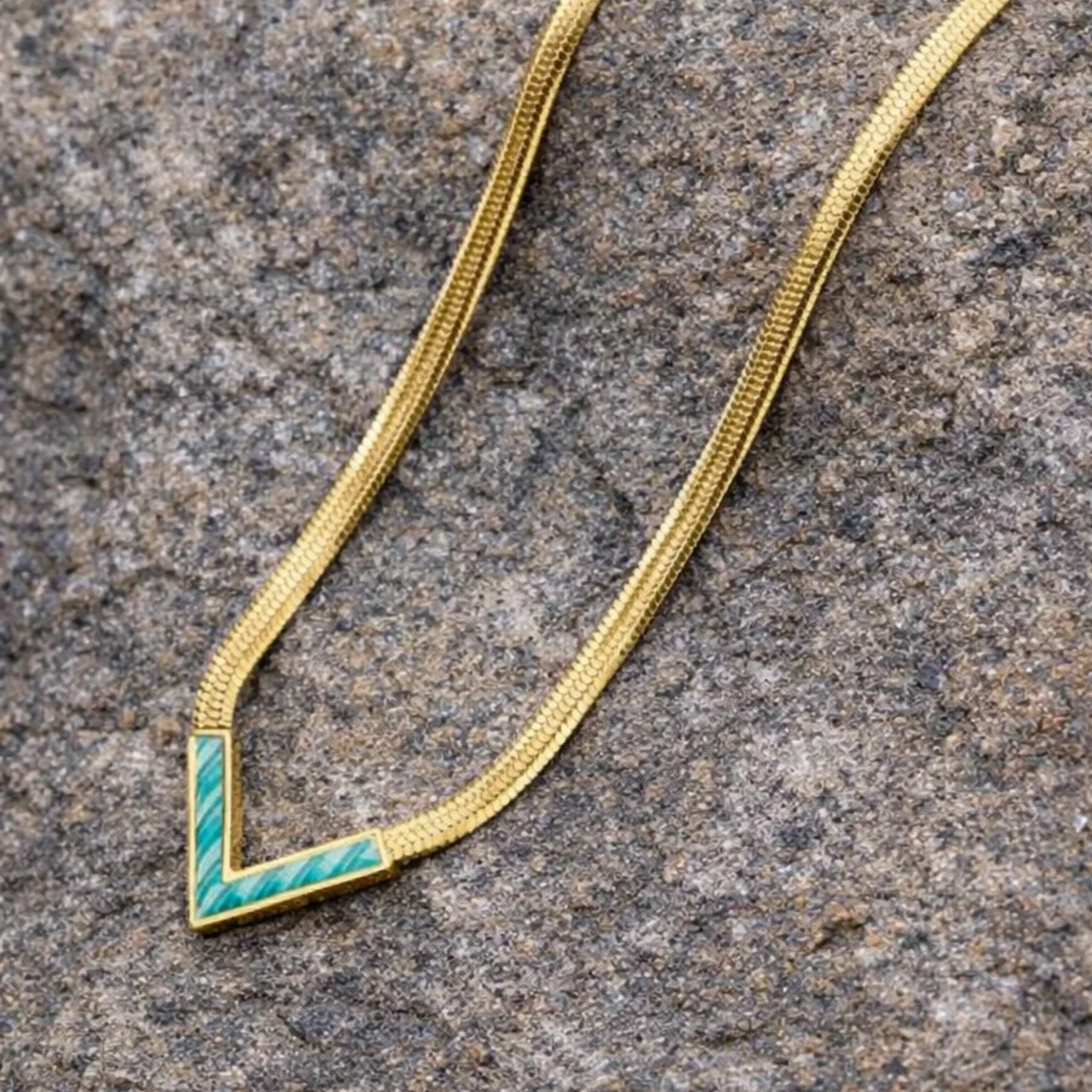Gold necklace with a green accent on a textured stone surface