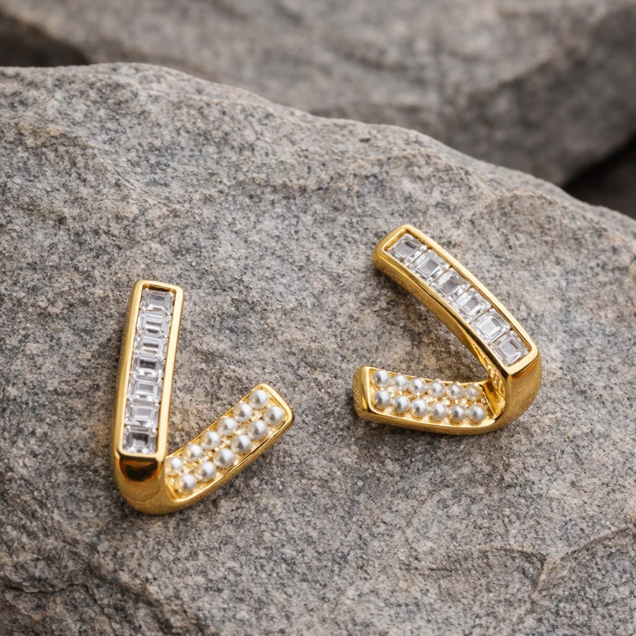 Gold 'V' shaped earrings with gemstones on a stone surface