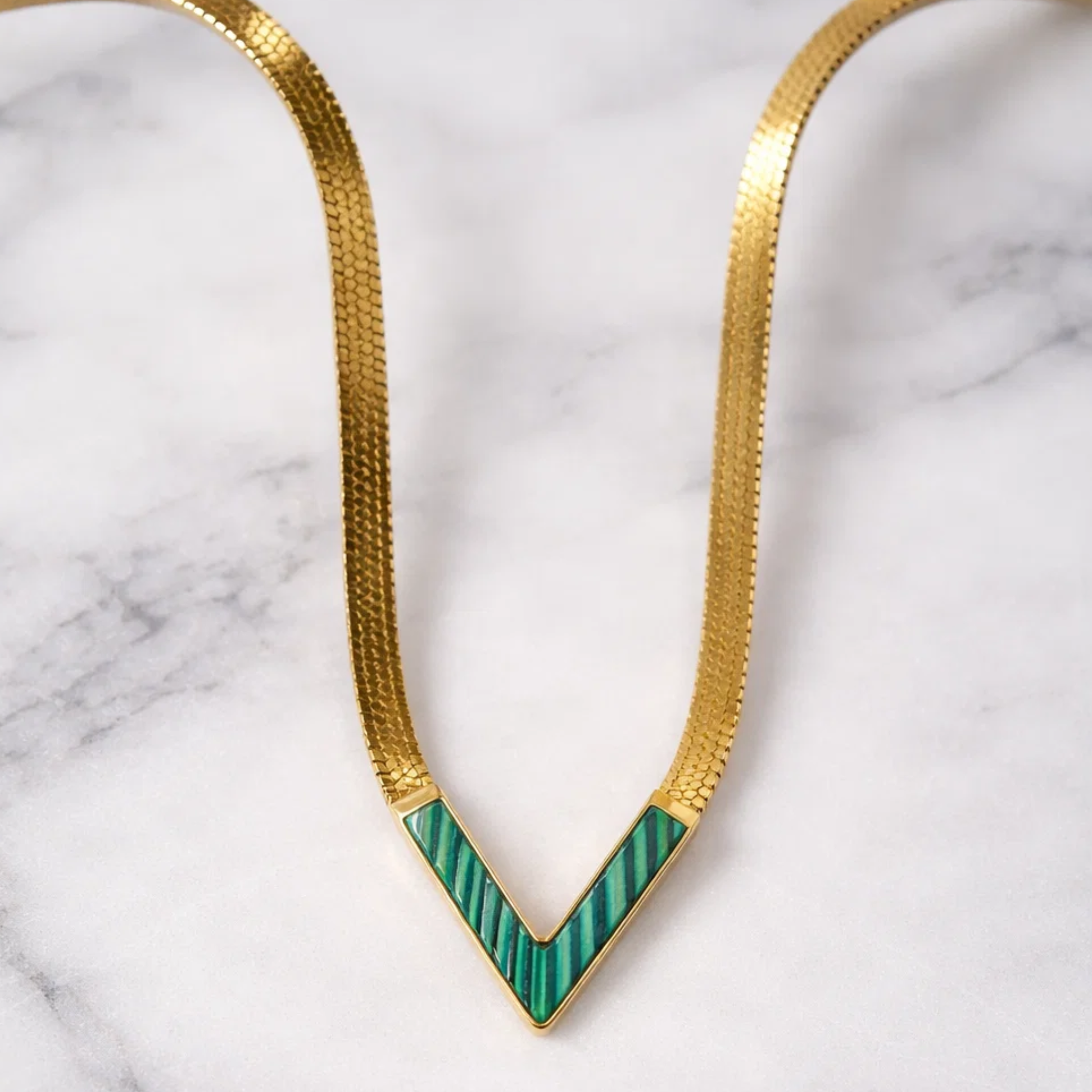 Gold necklace with green chevron design on a marble background