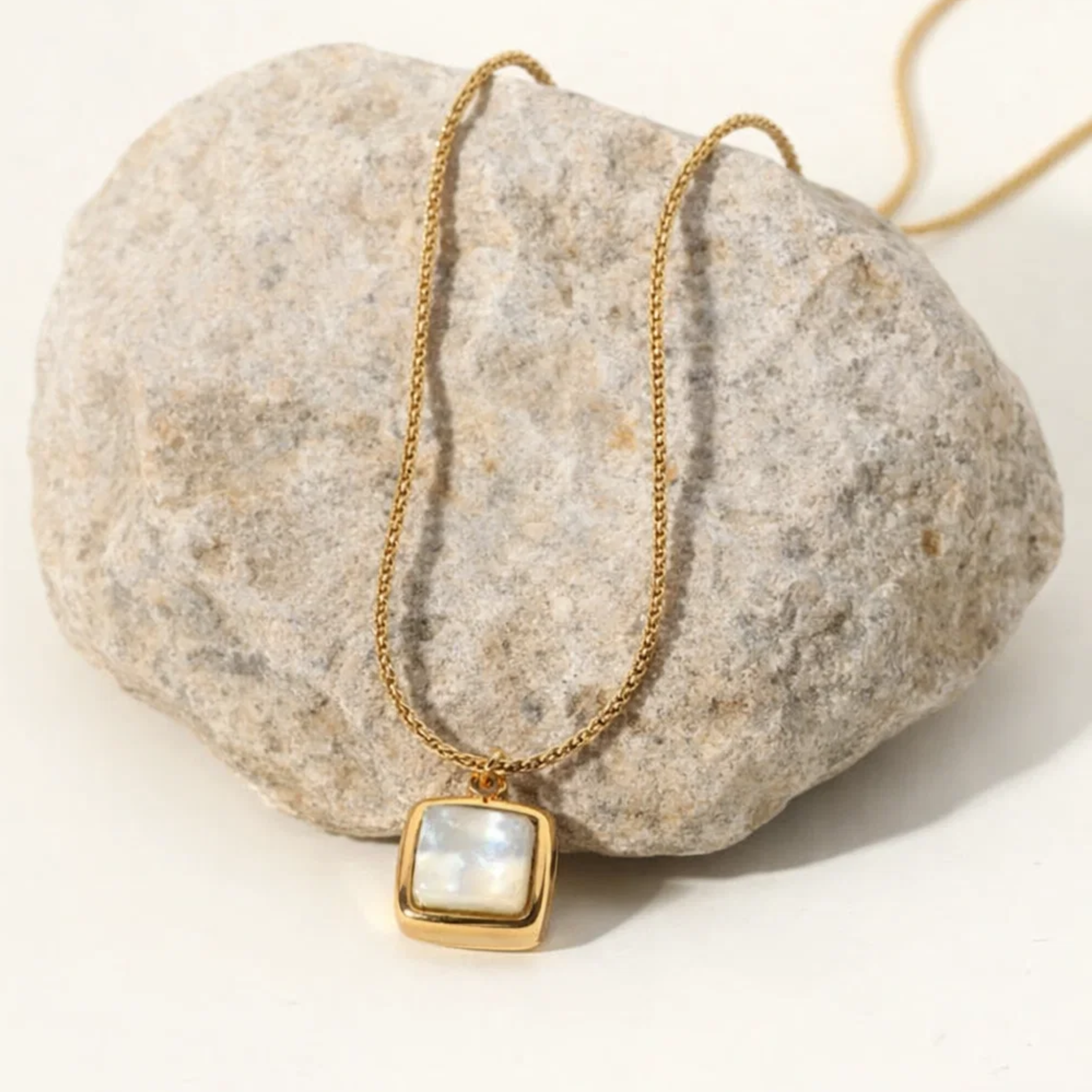 Gold necklace with a square pendant on a rock