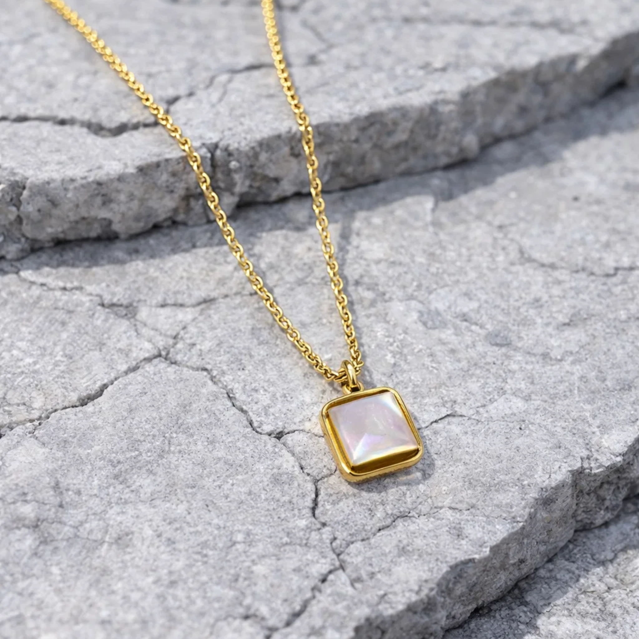 Gold necklace with a square pendant on a stone surface