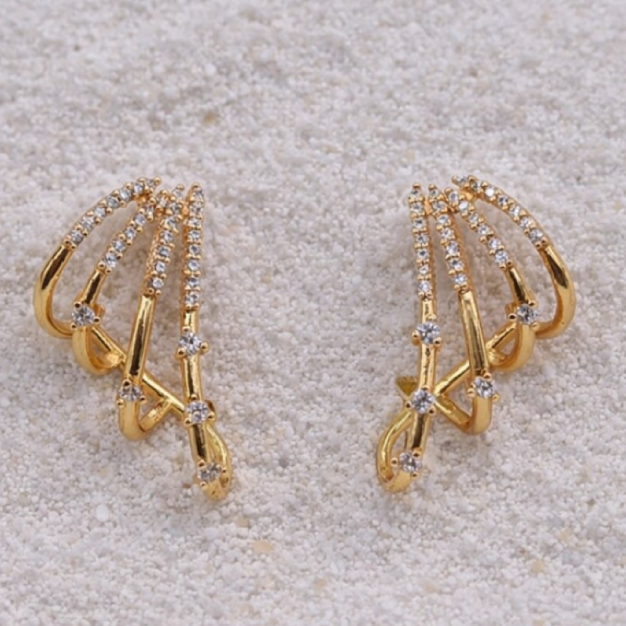 Gold earrings with diamond-like stones on a textured beige surface